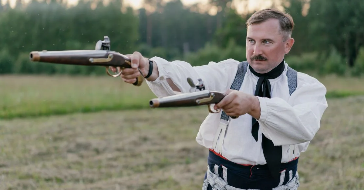 Homme en tenue traditionnelle visant des pistolets à silex de réplique en plein air.