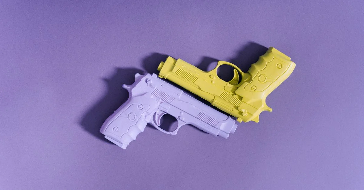 Des pistolets jouets violets et jaunes disposés sur une surface violette, formant un flat lay ludique.